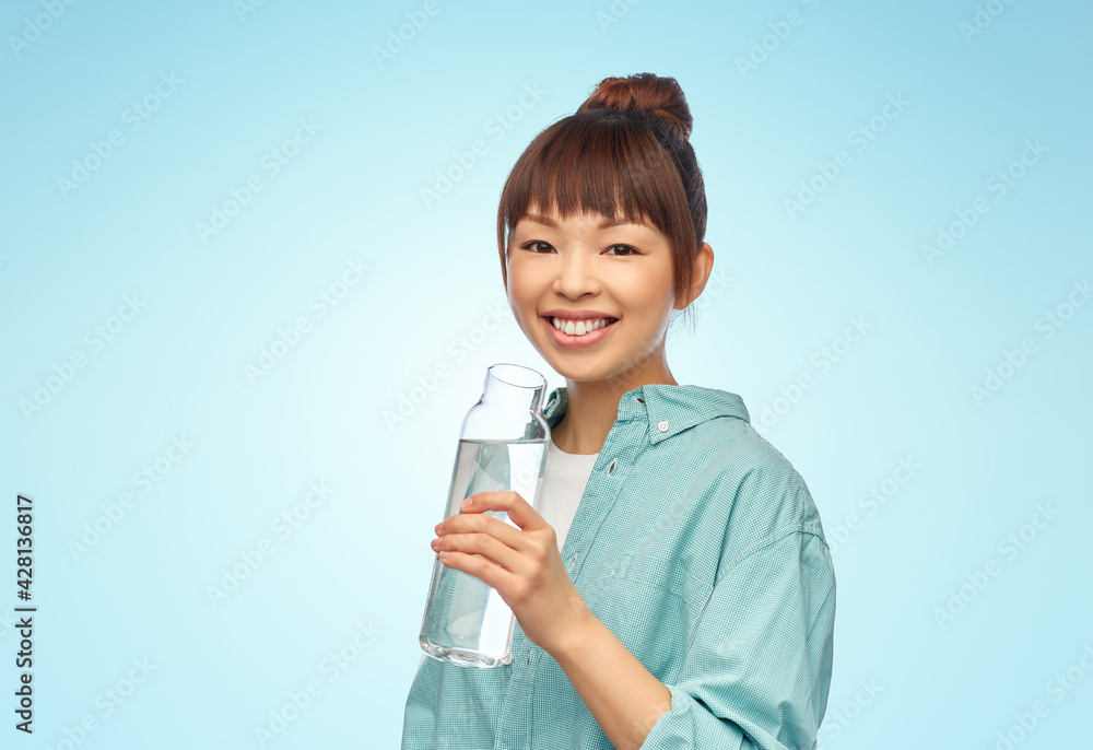 people concept - portrait of happy smiling young asian woman in turquoise shirt holding reusable glass bottle with water over blue background people concept - portrait of happy smiling young asian woman in turquoise shirt holding reusable glass bottle with water over blue background