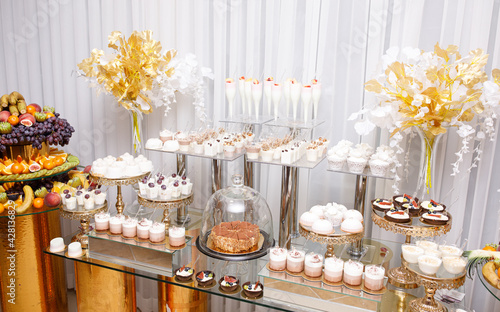Wedding Candy Bar with a large three-story cake in a classic style. Table with sweets and desserts for guests at the holiday. White sweet desserts are not harmful to the figure. 