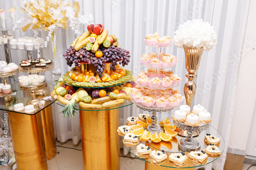 Wedding Candy Bar with a large three-story cake in a classic style. Table with sweets and desserts for guests at the holiday. White sweet desserts are not harmful to the figure. 