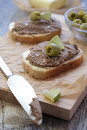 Breakfast: bread with chicken liver pate served with a slice of lime and green olive on wooden background.