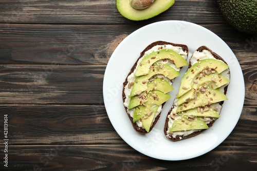 Avocado sandwich on dark rye bread made with fresh sliced avocados on brown background.