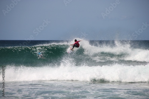 A young, sporty dark tanned male surfer in dynamic motion riding down the lip of a beautifully clear turquoise wave of medium size at Ocean Beach near Whangarei Heads, New Zealand