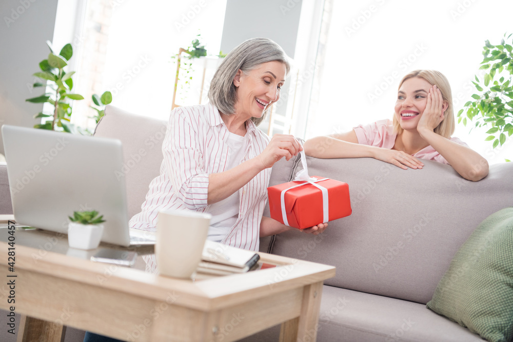 Photo of cheerful happy charming family sit sofa mother get gift daughter smile indoors inside house home Photo of cheerful happy charming family sit sofa mother get gift daughter smile indoors inside house home