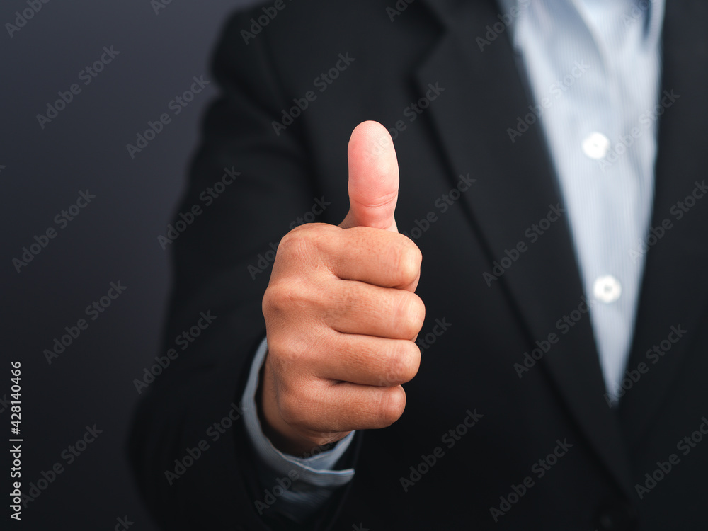 Businessman showing thumbs up like hand sign gesture against a gray color background. Happy confident man gesture. Space for text. Success in business Businessman showing thumbs up like hand sign gesture against a gray color background. Happy confident man gesture. Space for text. Success in business