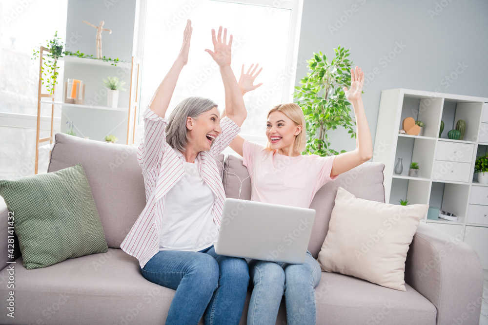 Photo of triumphant old woman and blonde young lady raise hands winner hold computer indoors inside house Photo of triumphant old woman and blonde young lady raise hands winner hold computer indoors inside house