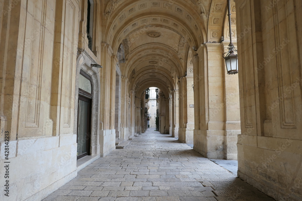 Valletta, Malta, March 17, 2021: Well worn limestone paving and ornate arches in the arcade at the front of the National Library of Malta. Valletta, Malta, March 17, 2021: Well worn limestone paving and ornate arches in the arcade at the front of the National Library of Malta.
