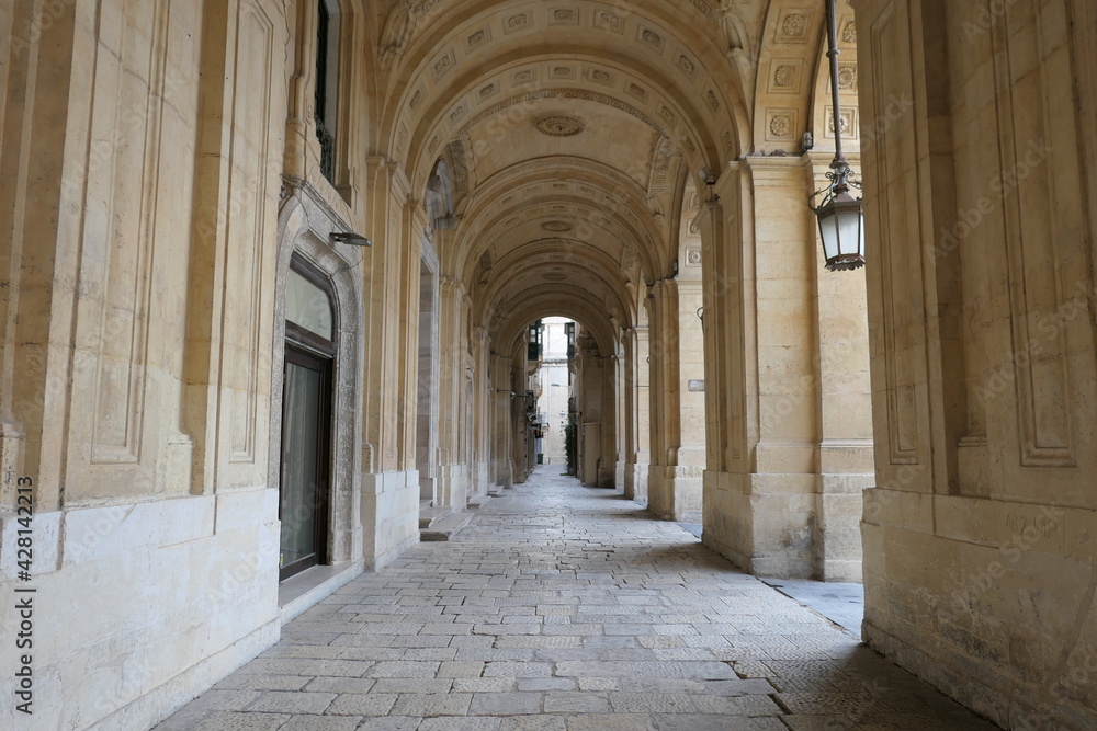 Valletta, Malta, March 17, 2021: Well worn limestone paving and ornate arches in the arcade at the front of the National Library of Malta.