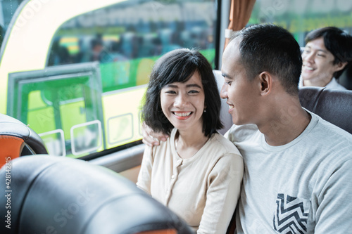 an asian man and woman chatting and laughing while sitting on the bus while traveling