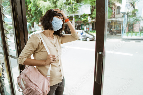 Asian woman wearing a mask stands waiting for the bus at the bus stop on a hot day