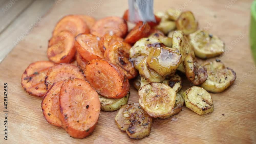 A young man greases grilled vegetables with garlic oil. A wooden eco-friendly tray. Vegetarian, outdoor recreation, patio. Carrot and zucchini. A young man greases grilled vegetables with garlic oil. A wooden eco-friendly tray. Vegetarian, outdoor recreation, patio. Carrot and zucchini.