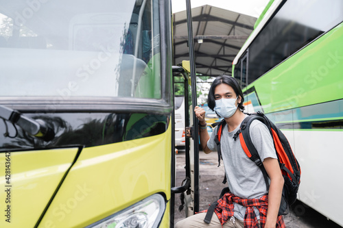 Potrait asian young man wearing face masks getting on the bus.A man wearing a face mask and carrying a backpack gets on the bus at the terminal