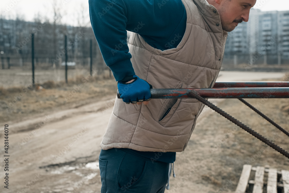Young man in sports gloves exercising on the uneven bars outside. Cropping. Power workout outdoors Young man in sports gloves exercising on the uneven bars outside. Cropping. Power workout outdoors