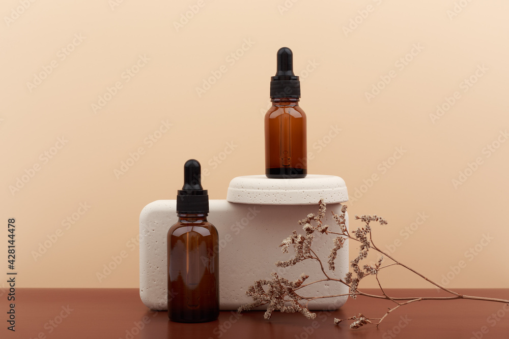 Two skin serum with stone geometric forms and dry flower on dark brown table against beige background. Concept of beauty products for anti acne, anti aging or moisturizing products for healthy skin