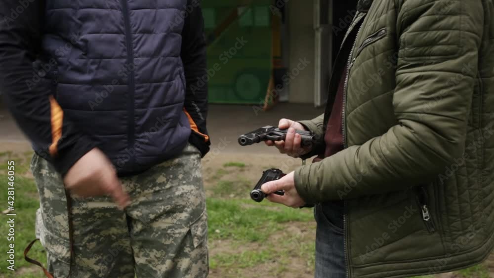 A young man talks to an instructor. Explains safety techniques and ways to fire a gun. shooting gallery. Sports shooting, hobbies, firearms dangerous weapons. outdoor activity dark A young man talks to an instructor. Explains safety techniques and ways to fire a gun. shooting gallery. Sports shooting, hobbies, firearms dangerous weapons. outdoor activity dark
