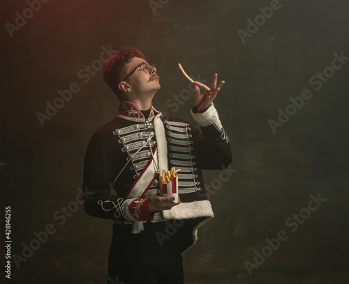 Young man in suit as royal person isolated on dark green background. Retro style, comparison of eras concept. Beautiful male model like historical character, monarch, old-fashioned. photo