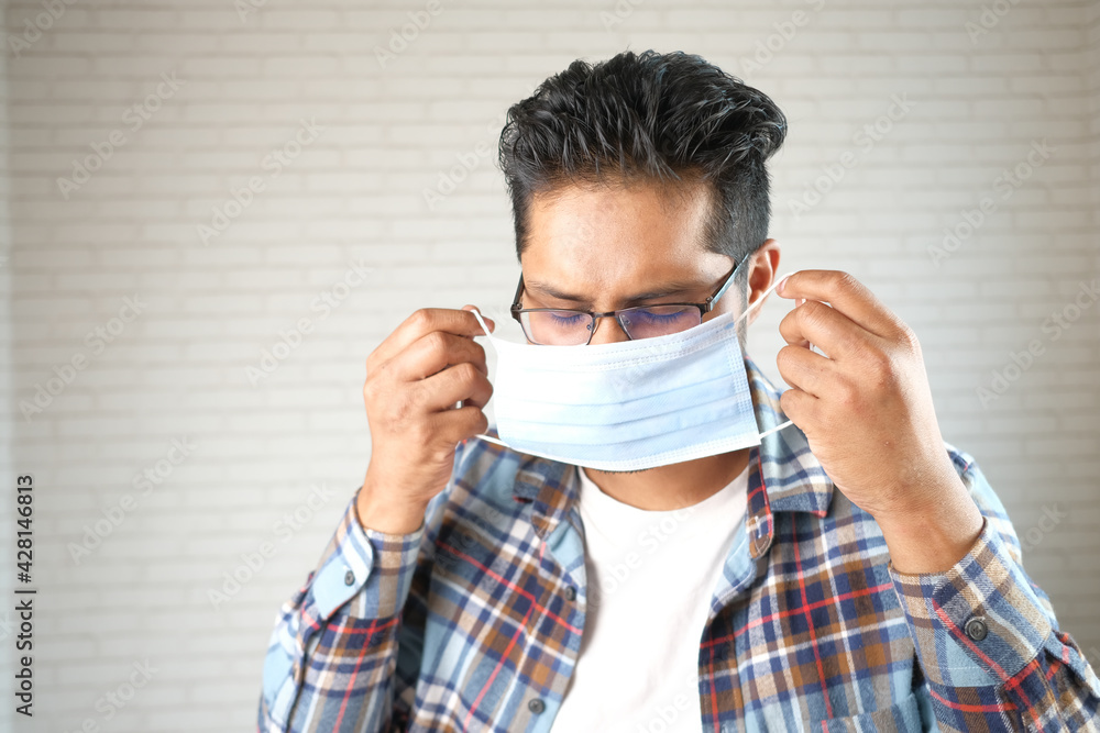 young asian man putting surgical face mask indoor young asian man putting surgical face mask indoor