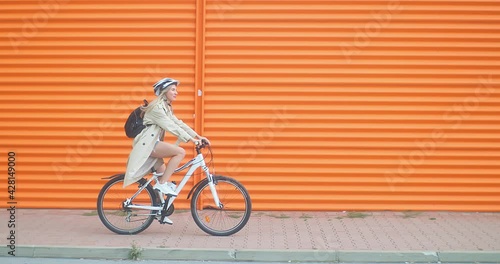 Woman bicyclist in helmet riding on orange background in the city on sport retro bike. 4K video.
