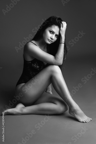 Stylish black lingerie on fit young female model sitting on red studio background, copy space for underwear advertising
