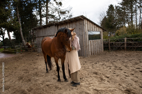 Eine blonde Frau aus den Mittelalten Zeiten kuschelt mit ihrem Pferd. Sie hat Fell auf den Schultern, ein Rock aus beige Decke. Sie kommt aus dem Dorf und steht vom Stahl.sie umarmen sich.