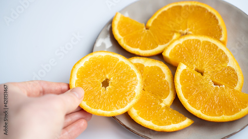 Hand picking a slice of orange from the plate on the table. Orange slice at the hand. Juicy orange on a gray plate