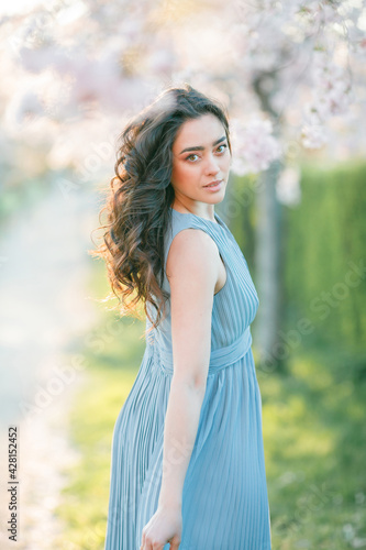 Beautiful young woman with curly hair is resting in the blooming sakura garden.