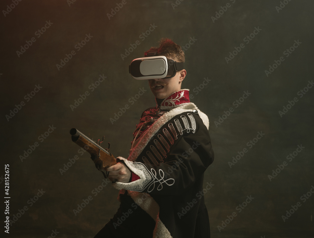 Fototapeta premium Young man in suit as royal person isolated on dark green background. Retro style, comparison of eras concept. Beautiful male model like historical character, monarch, old-fashioned.