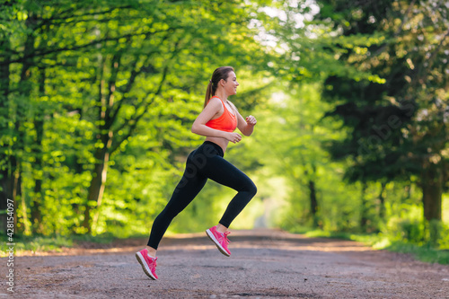 Athletic fit runner woman running in the park with trees in the