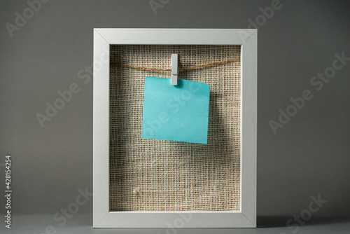 White frame with hanging chit on the clip and the cord and linen background.