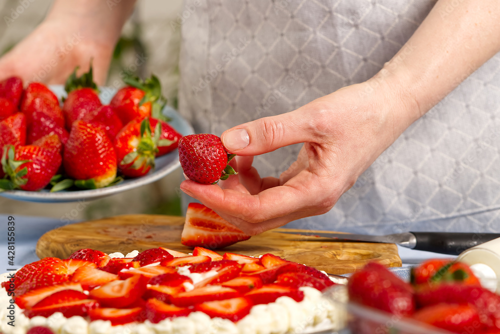 woman baker stacks strawberries on meringue strawberry cake base. Homemade strawberries cake made from meringue cake and cream with strawberries. home cooking concept woman baker stacks strawberries on meringue strawberry cake base. Homemade strawberries cake made from meringue cake and cream with strawberries. home cooking concept