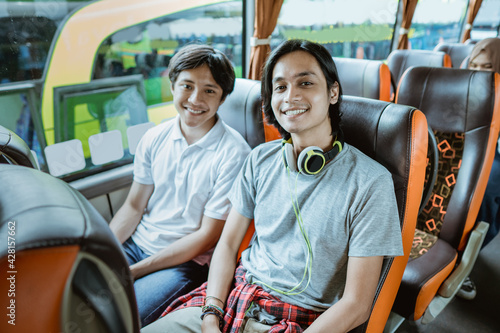 a young Asian boy and a man with headphones smiling into the camera while sitting by the window on the bus