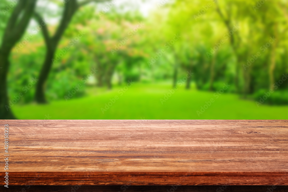 Wooden table with Blurry image of green grass meadow field and green trees in background. Wooden table with Blurry image of green grass meadow field and green trees in background.