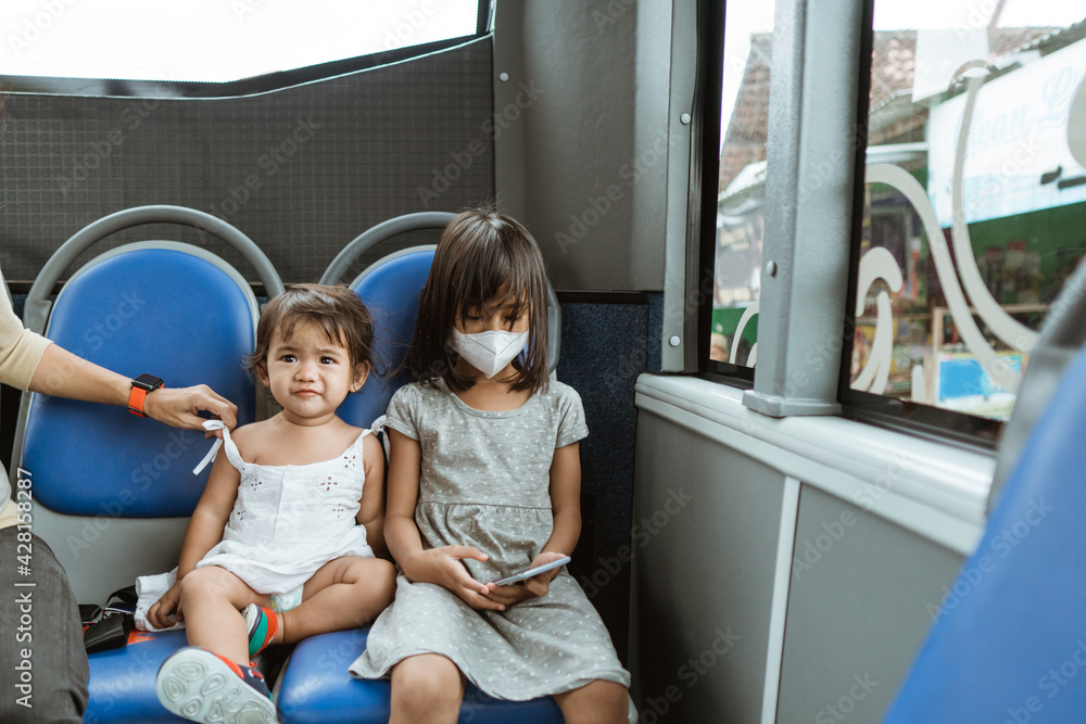two cute little girls sitting on a bench holding a cellphone on the bus while traveling