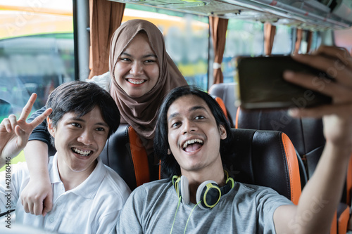 Three friends smile and pose in front of their cellphone camera while taking selfies together on the bus © Odua Images