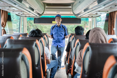 A bus crew in uniform and a hat briefs the passengers on the bus before leaving