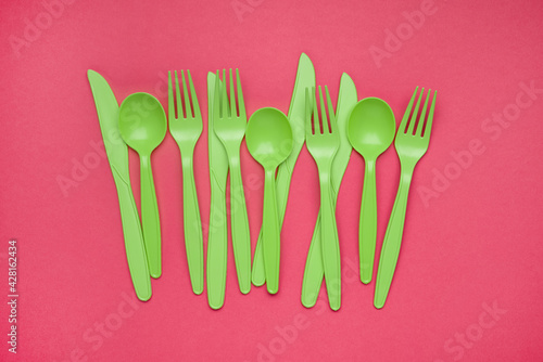 Green plastic forks, spoons, knifes on pink paper. Set of plastic cutlery in different spoons forks knives and eco-friendly plastic concept. Flat lay. Horizontal. Close-up. photo