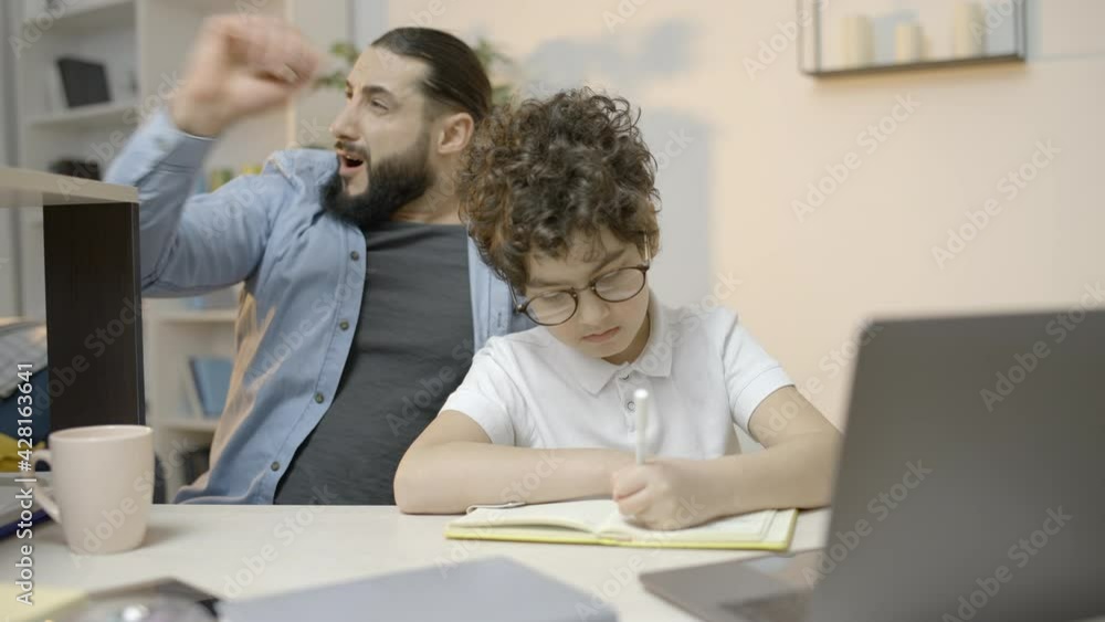 Bored father yawning controlling little son doing home assignment, studying Bored father yawning controlling little son doing home assignment, studying