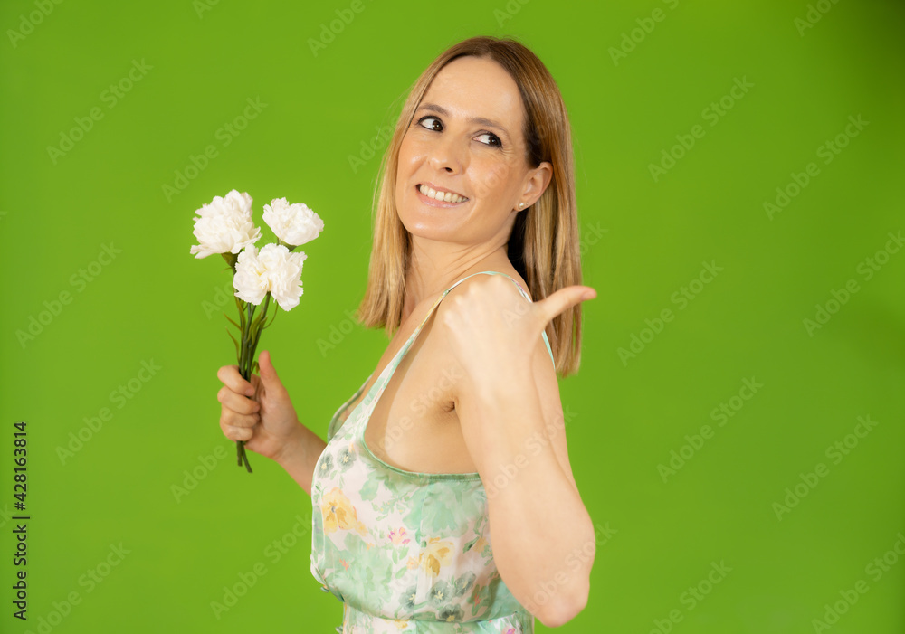 Portrait of a smiling playful cute woman holding flowers with thumb up isolated over green background