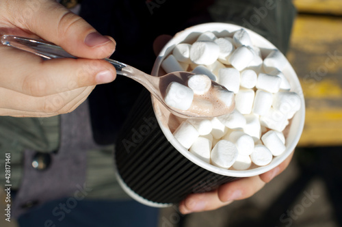 Child's hands with paper cup of cocoa with marshmallows on street