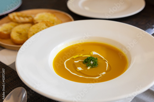 Close up and selective focus shot of pumpkin soup with vibrant orange color and luxury decoration in white plate shows warm dinner with family in thanksgiving day which is sharing meal for happiness.