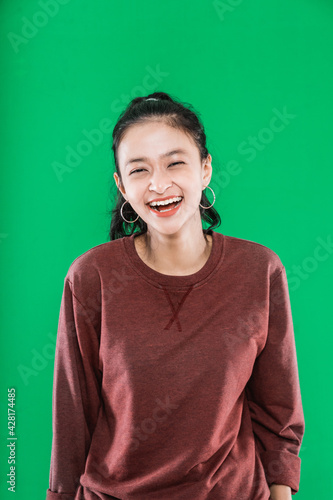 Beautiful young asian woman wearing sweater while laughing and looking at camera isolated on green background