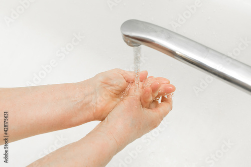 Elderly woman washes her hands under the tap in the bathroom. Domestic hygiene photo