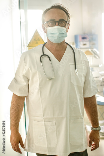 Dottore in camice bianco e mascherina chirurgica guarda serio dalla sala di un ospedale 
 photo