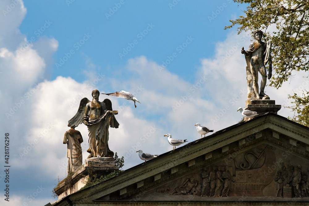 Detail of the classical temple in the center of the small lake of Villa Borghese in Rome, marble statues, seagulls and blue sky with cloud