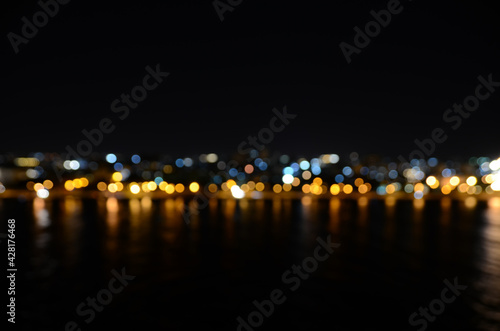Bokeh of night coastline scene. Blur effect from the water and city lights in the background reflecting in the water. Defocused city skyline in front of the ocean.