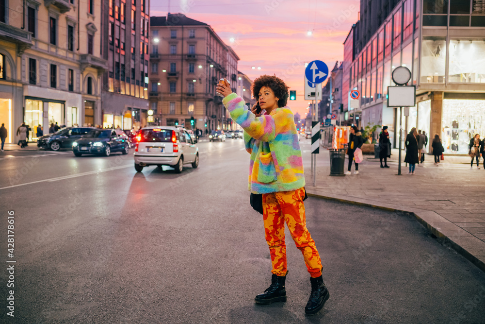 Young afro woman talking smartphone raising hand calling taxi hitchhiking in the city