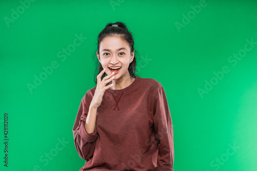 young Asian woman expressing happy wide-open mouth and raising hands on the chin isolated on green background