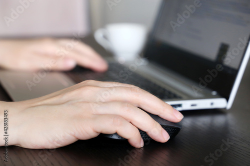 Female hands on laptop keyboard and computer mouse. Woman works with docs sitting at the wooden desk