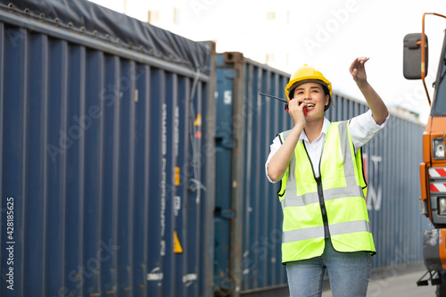 woman factory worker or engineer using walkie talkie and calling someone for preparing a job in containers warehouse storage
