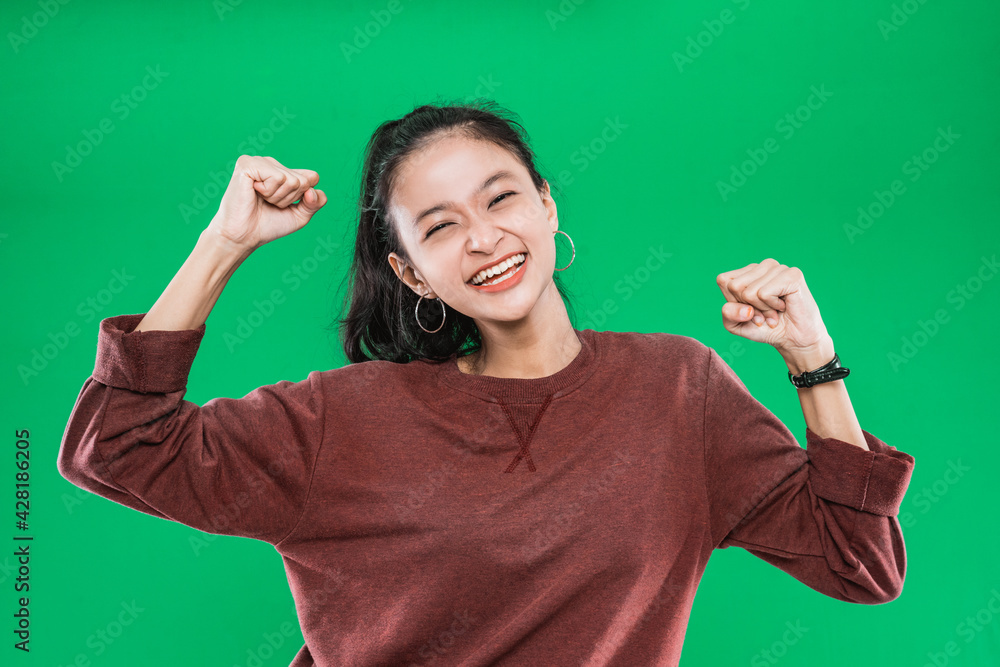 Asian young girl smiling happy while clenched into fists and raised two hands isolated on a green background Asian young girl smiling happy while clenched into fists and raised two hands isolated on a green background