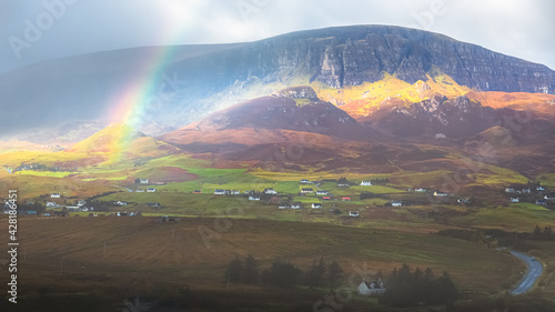 Moody  dramatic light and shadow with a colourful rainbow over the rural countryside landscape of the Quiraing at Trotternish ridge above Staffin village on the Isle of Skye  Scotland.